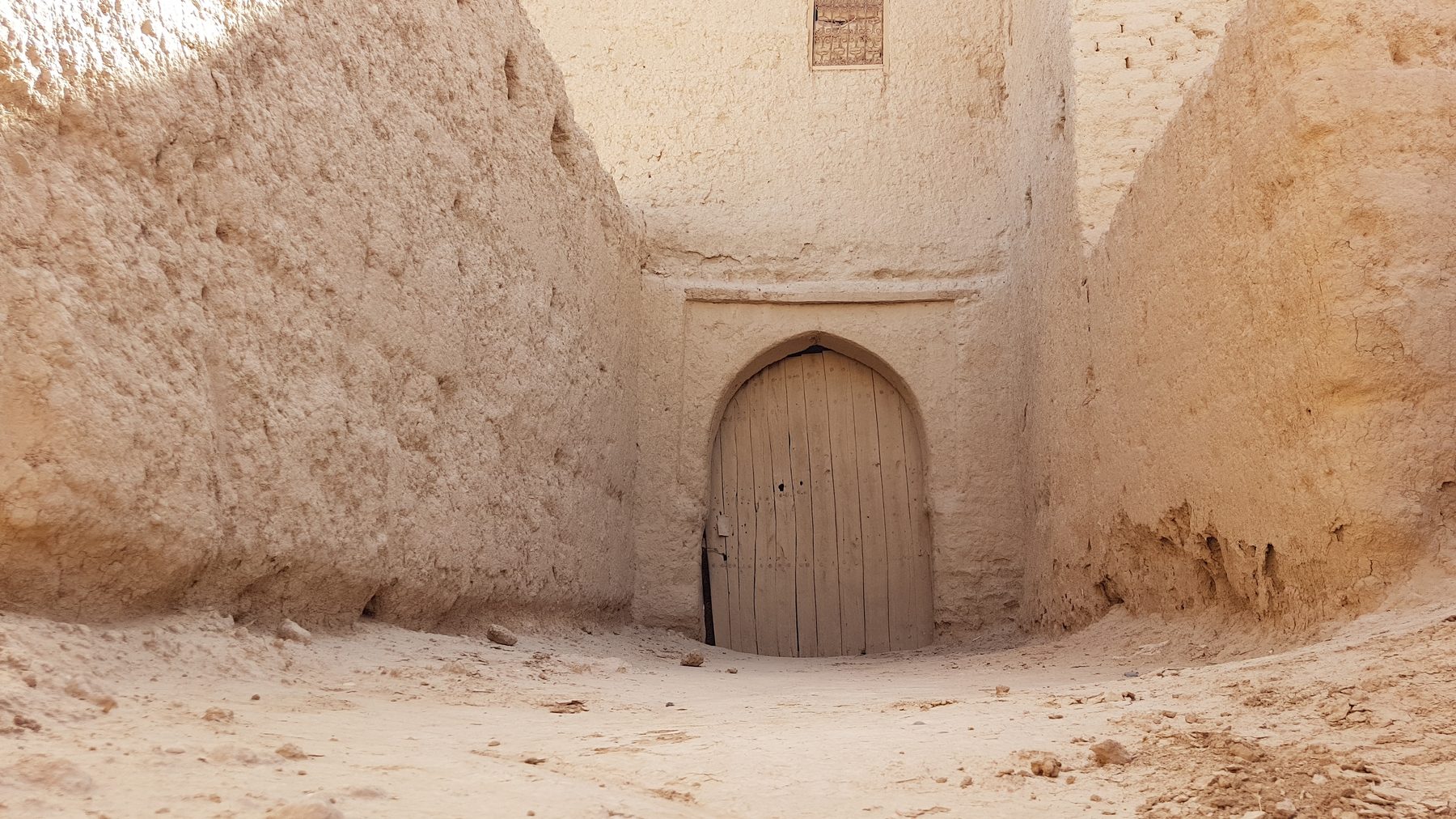 An arched wooden door closed within thick earthen walls